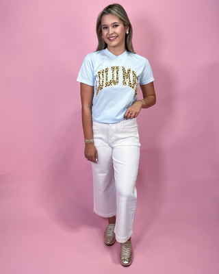 Person wearing a light blue t-shirt with gold text and white pants on a pink background
