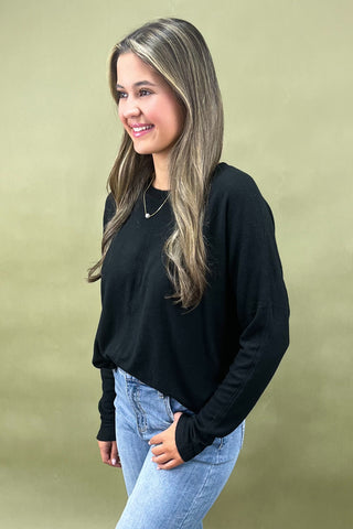 Woman wearing a black long-sleeve top and light blue jeans against a beige background