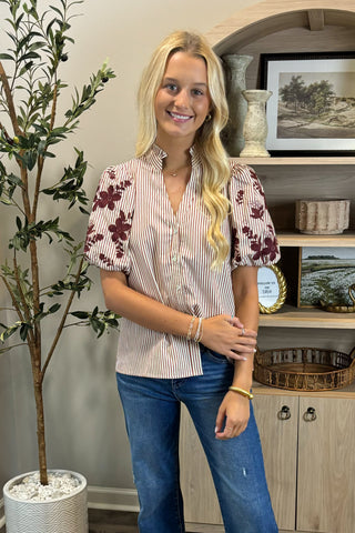 Woman wearing a patterned blouse and jeans standing in a room with decor elements.
