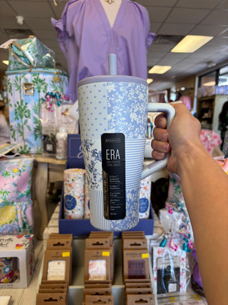 Person holding a blue floral-patterned mug with 'ERA' branding in a store setting.