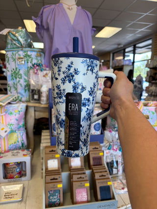 Hand holding a blue and white floral-patterned mug with 'ERA' branding in a store setting.