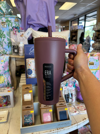 Person holding a brown mug with a straw lid in a store setting