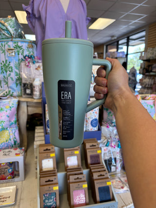 Hand holding a green mug with 'ERA' branding in a store setting