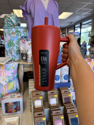 Red mug with 'ERA' branding held by a person in a store setting.