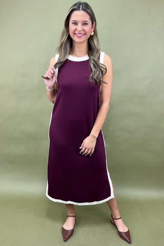 Woman wearing a maroon dress with white trim against a green background