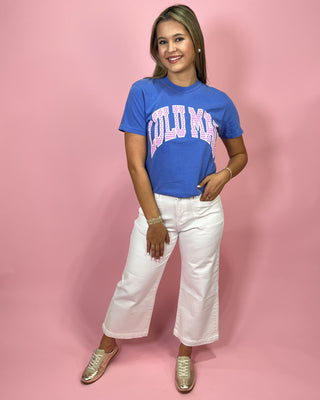 Person wearing a blue t-shirt with text and white pants on a pink background