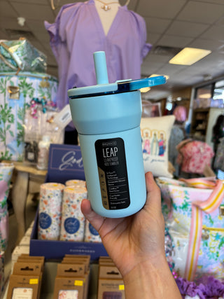 Light blue tumbler with a straw held in front of a store interior.