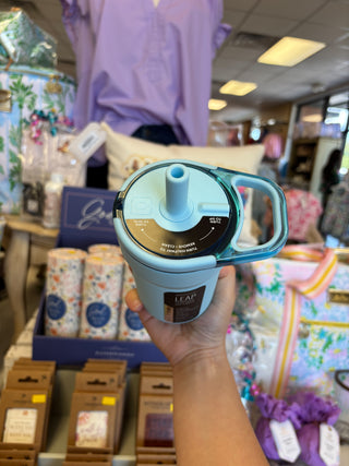 Hand holding a blue and black tumbler with a handle in a store setting