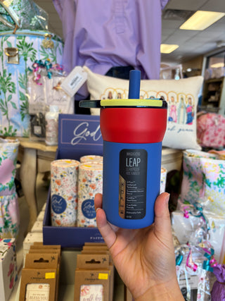 Blue and red insulated tumbler with straw held in a store setting