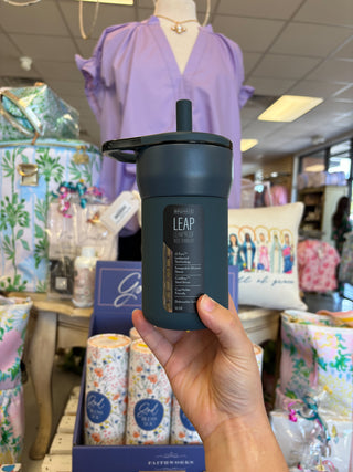 Person holding a dark blue tumbler with 'LEAP' branding in a store setting.