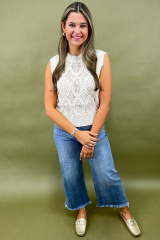 Woman wearing a white sleeveless top and blue jeans against a green background