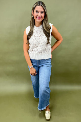 Woman wearing a white sleeveless knitted top and blue jeans on a green background