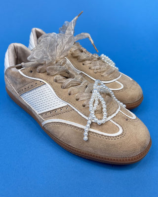 A pair of beige suede sneakers with white mesh panels, white laces decorated with pearl-like beads