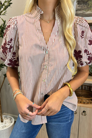 Person wearing a striped shirt with floral patterns and blue jeans indoors.