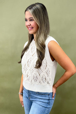Woman wearing a white lace sleeveless top and blue jeans against a green background