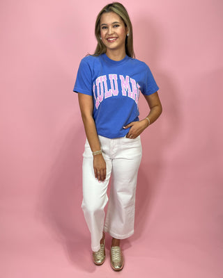 Woman wearing a blue t-shirt with pink text and white pants on a pink background