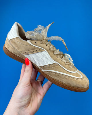 A pair of beige suede sneakers with white mesh panels, white laces decorated with pearl-like beads