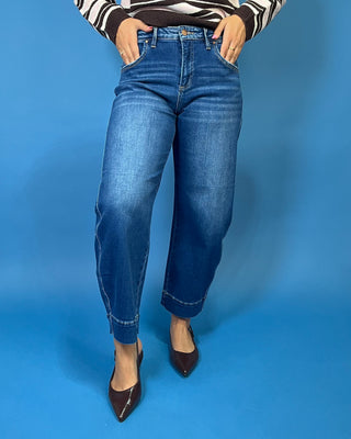 A person wearing medium-wash blue cropped jeans with a striped long-sleeve top and dark brown pointed-toe heels