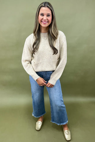 Woman wearing a beige sweater and blue jeans against a green background