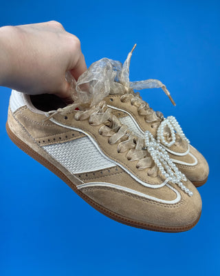 A pair of beige suede sneakers with white mesh panels, white laces decorated with pearl-like beads