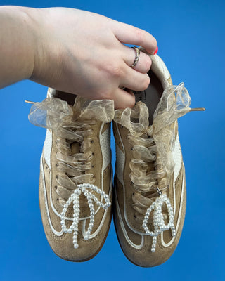A pair of beige suede sneakers with white mesh panels, white laces decorated with pearl-like beads