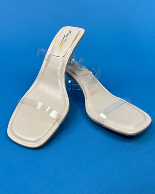 A pair of beige heeled slide sandals with clear transparent straps
