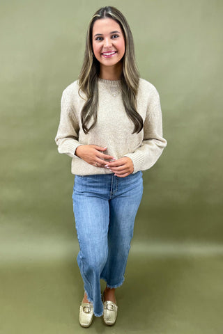 Woman wearing a beige sweater and blue jeans against a green background