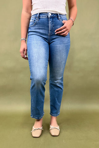 Person wearing blue jeans and a white top against a green background