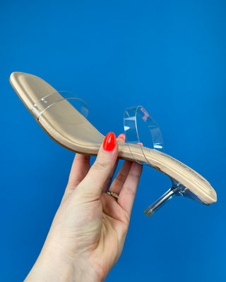 A pair of beige heeled slide sandals with clear transparent straps