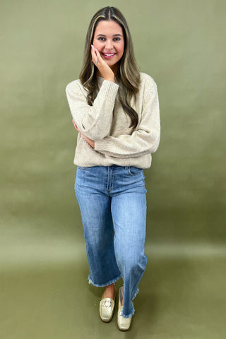 Woman wearing a beige sweater and blue jeans against a green background