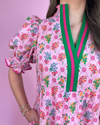Woman wearing a pink floral dress with green and pink accents against a pink background