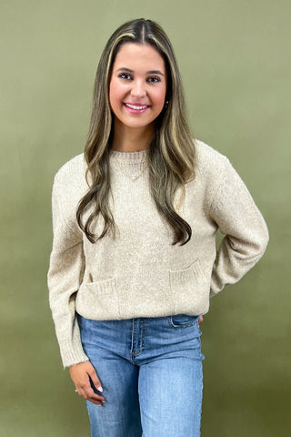 Woman wearing a beige sweater and blue jeans against a green background