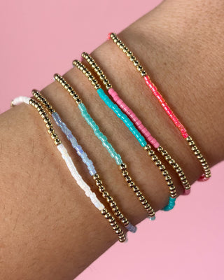 Wrist wearing multiple beaded bracelets on a pink background