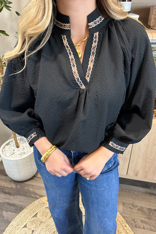 Person wearing a black blouse with lace details and blue jeans indoors.