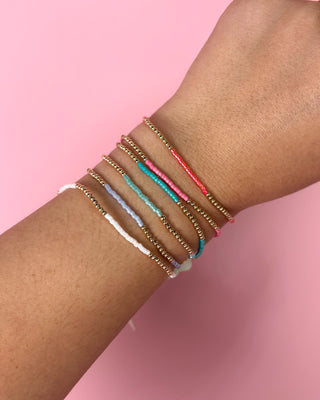 Close-up of a wrist wearing multiple colorful bracelets on a pink background