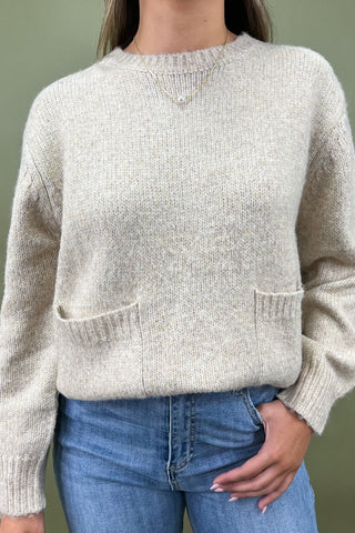 Person wearing a beige sweater and blue jeans against a green background