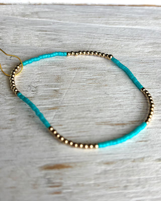 Turquoise beaded necklace with gold accents on a light wooden surface