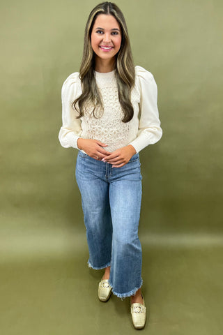 Woman wearing a white blouse, blue jeans, and beige shoes against a green background