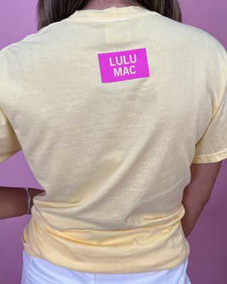 Yellow t-shirt with 'LULU MAC' logo on the back against a purple background