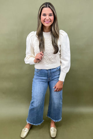 Woman wearing a white blouse with ruffled sleeves and blue jeans against a green background