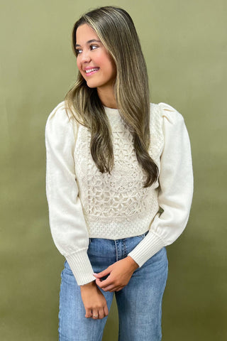 Woman wearing a white lace top and blue jeans against a green background