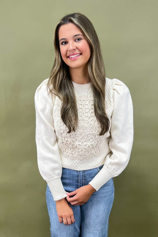 Woman wearing a white lace top and blue jeans against a green background