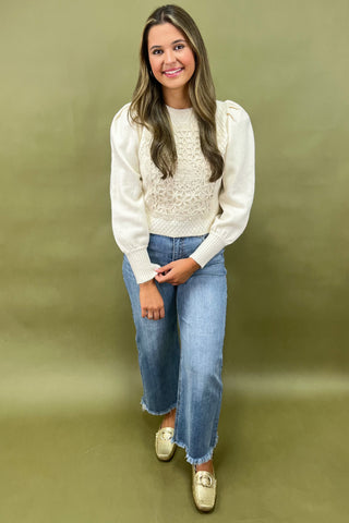 Woman wearing a white sweater with lace details and blue jeans on a green background
