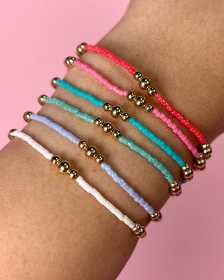 Set of colorful beaded bracelets on a wrist with a pink background