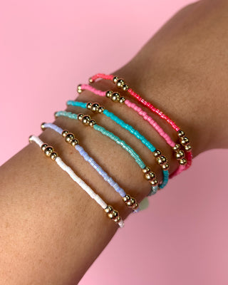 Multicolored beaded bracelets on a wrist with a pink background
