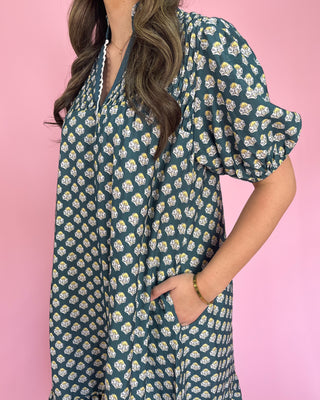 Woman wearing a teal floral dress against a pink background