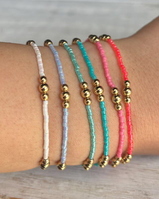 Five colorful beaded bracelets with gold beads on a wrist against a neutral background