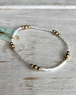 Beaded bracelet with gold and white beads on a light wooden surface