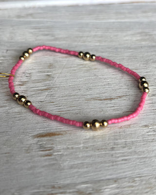 Bracelet with pink beads and gold accents on a wooden surface