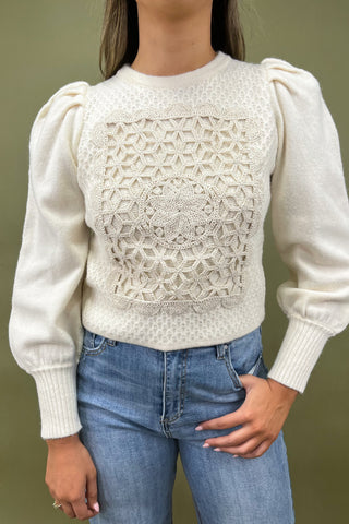 Person wearing a white sweater with geometric pattern and blue jeans against a green background